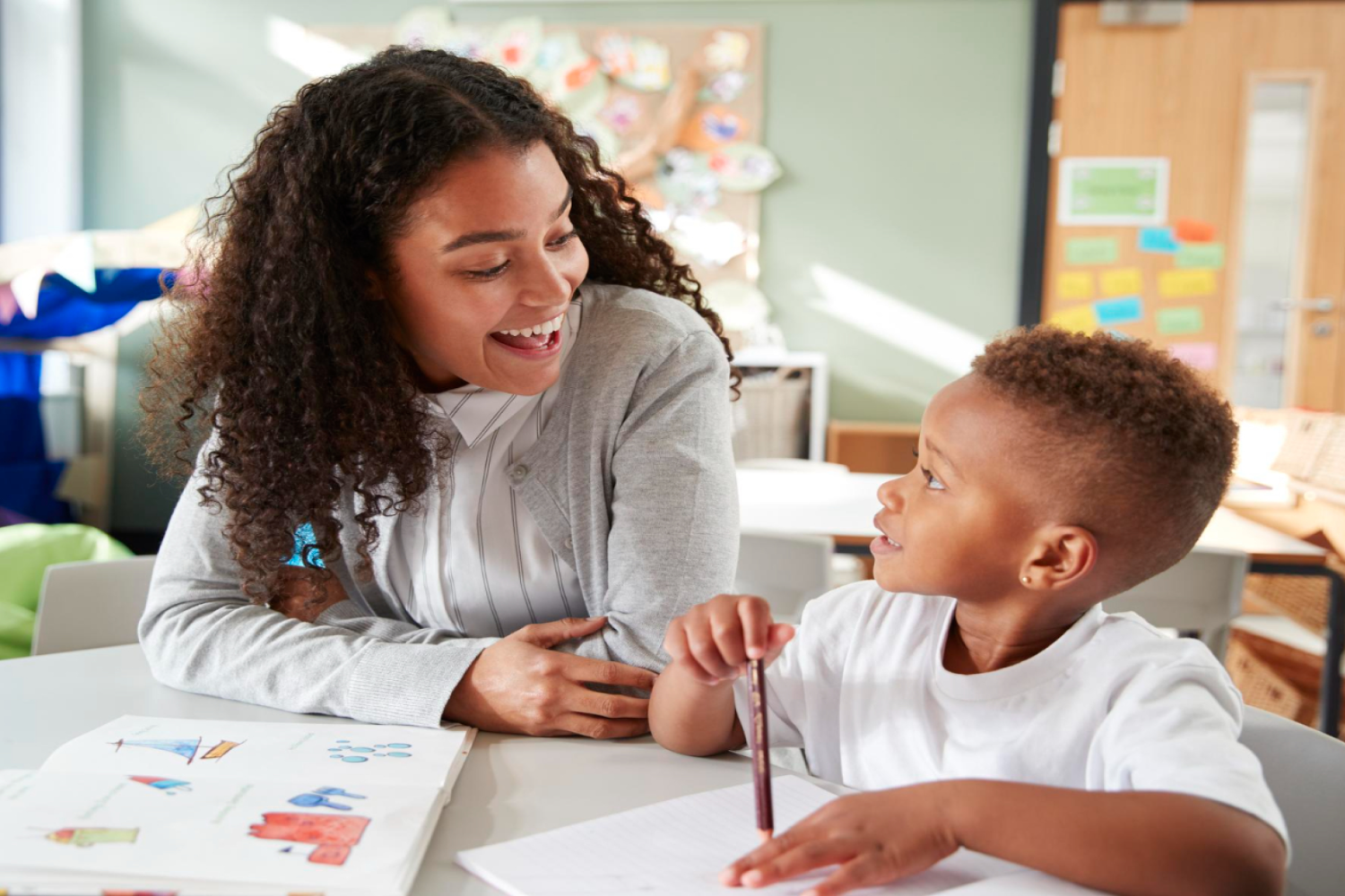 female-infant-school-teacher-working-one-one-with-young-schoolboy-sitting-table-smiling-each-other-close-up 12